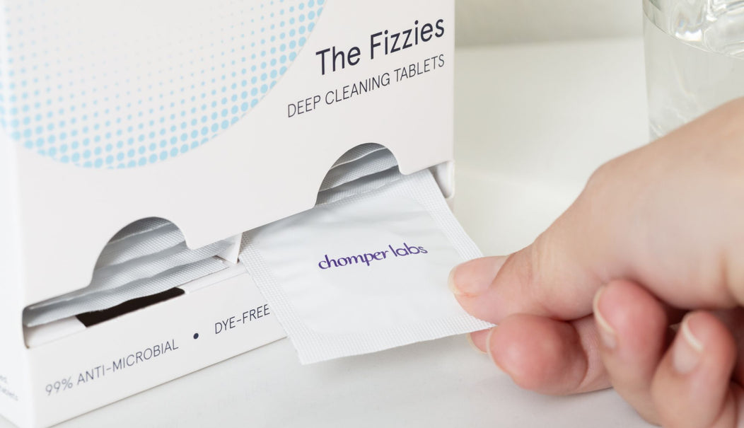 Hand pulling a single tablet of Chomper Labs The Fizzies deep cleaning tablets for night guards and retainers from the easy access opening on the box.